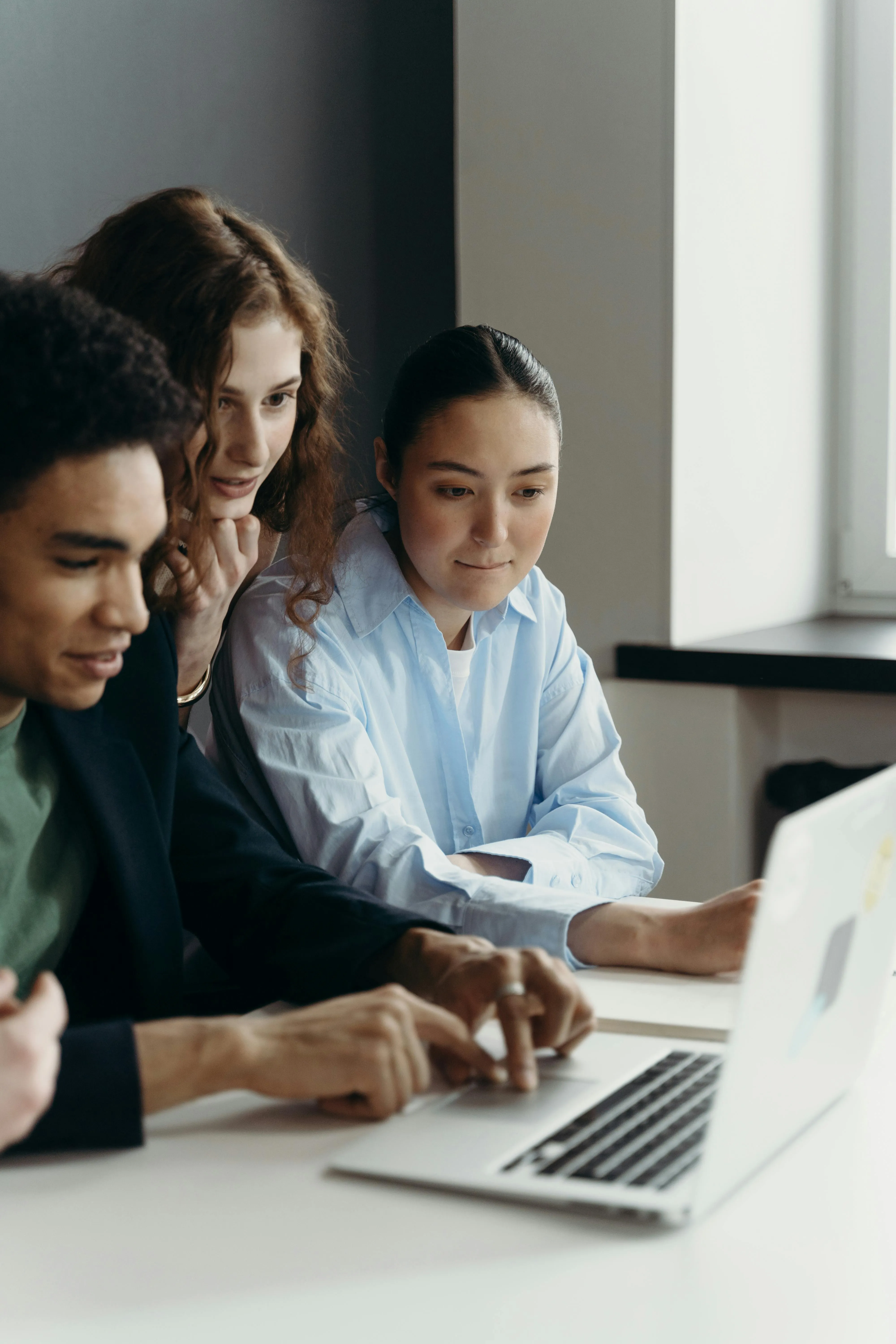 Three colleagues gathered around a laptop, exploring and discussing AI tools and their capabilities.