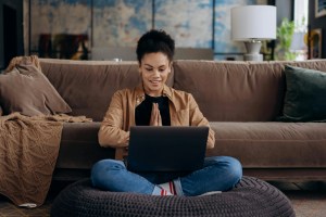Woman sitting on a sofa using her laptop, smiling while browsing a beautifully designed website.