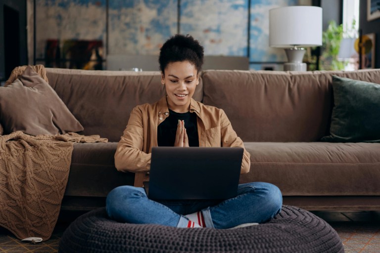 Woman sitting on a sofa using her laptop, smiling while browsing a beautifully designed website.