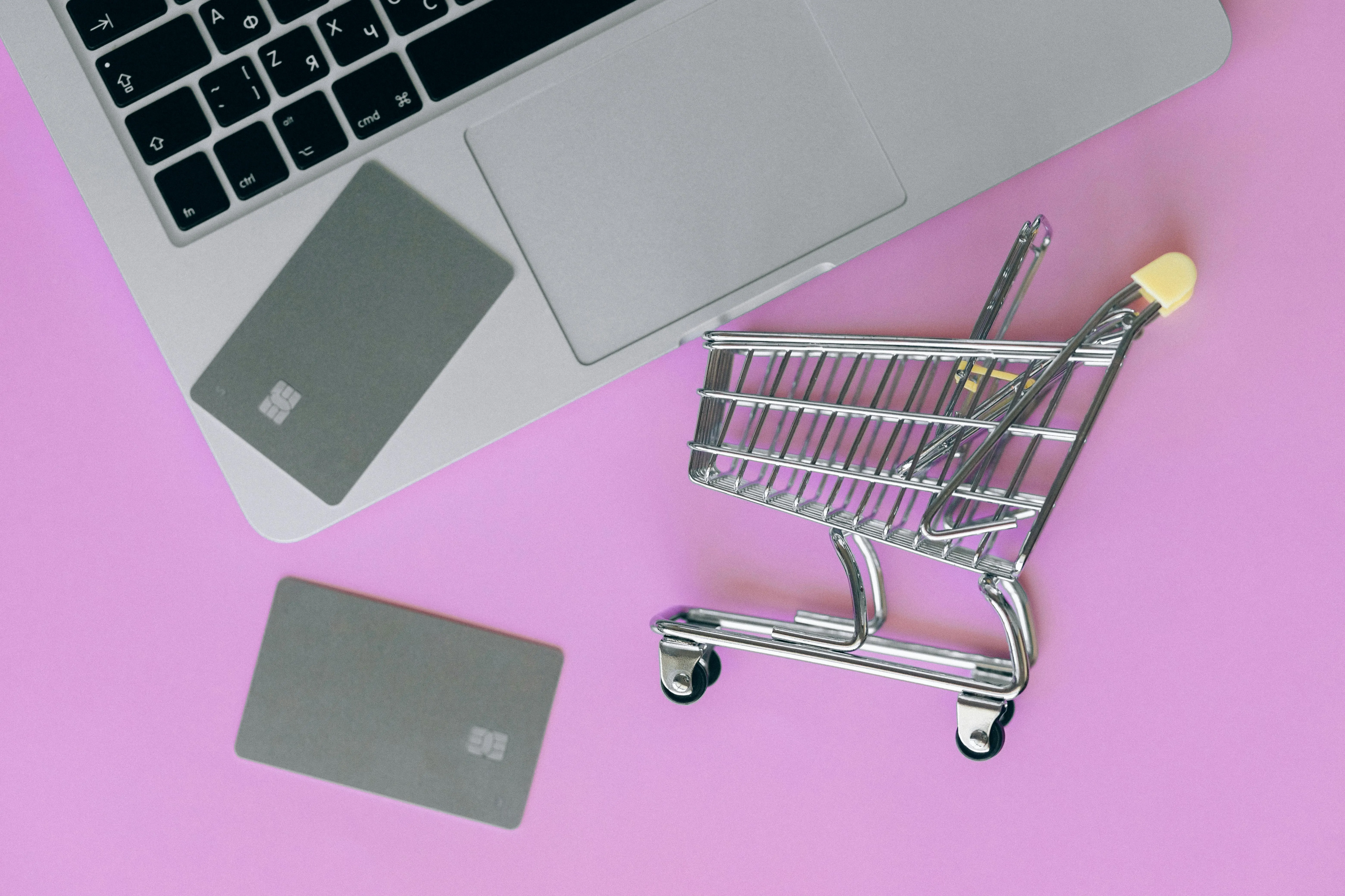 Pink table with a laptop, two credit cards, and a small shopping cart representing online payments and e-commerce